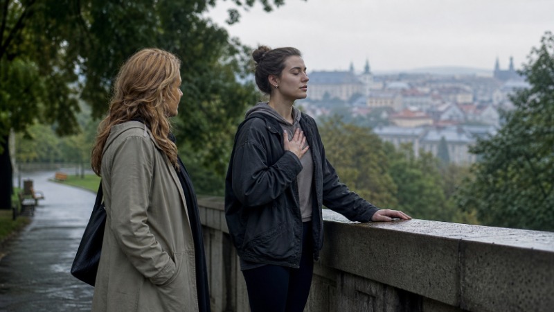 Žena sedí na posteli, objímá si kolena a zhluboka dýchá u pootevřeného okna